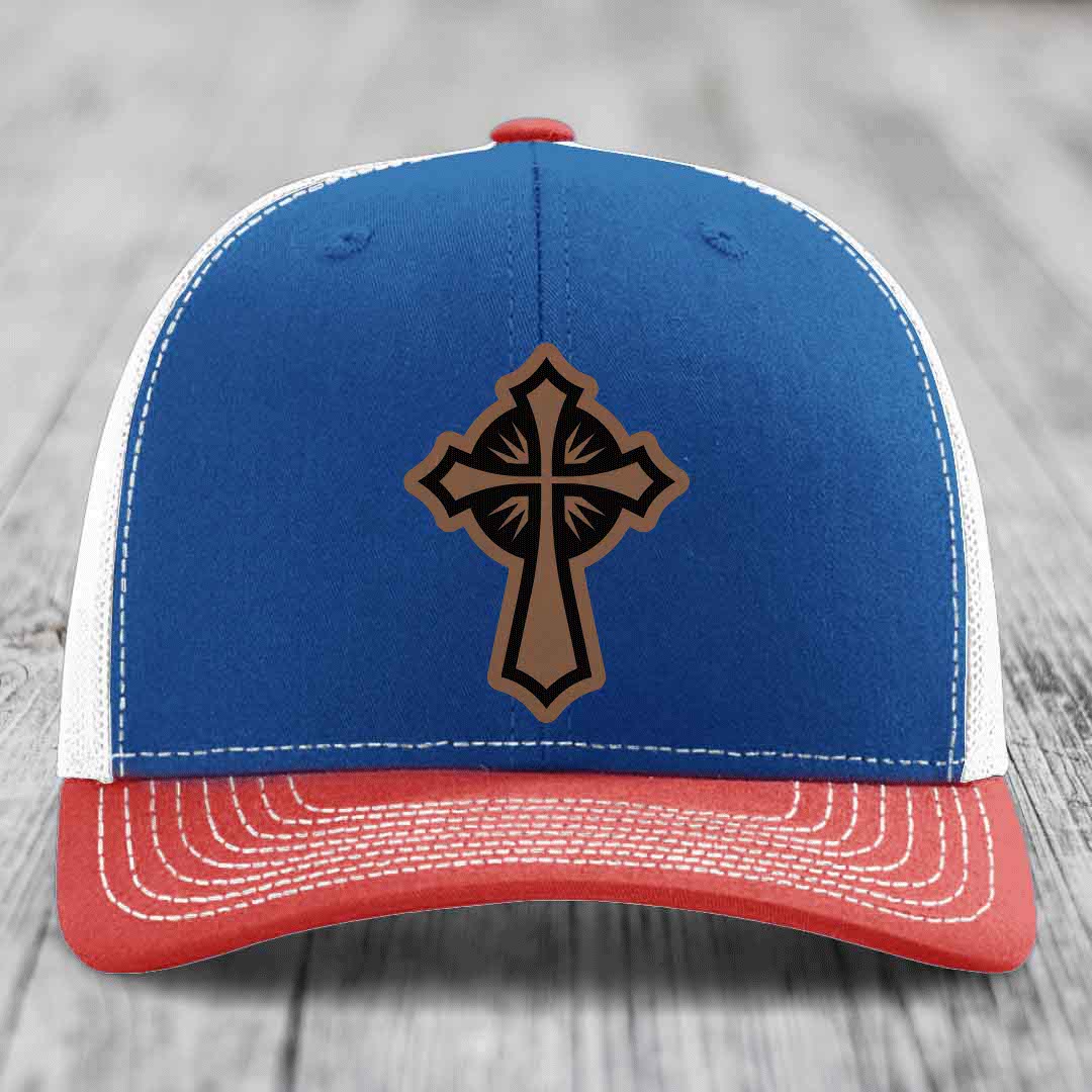 Blue and red trucker hat with a brown leatherette cross patch on the front.