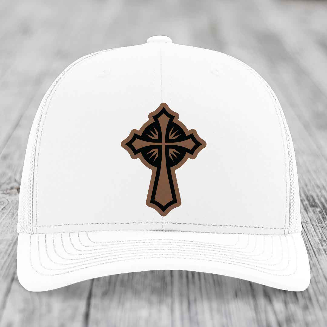 White trucker hat with a brown and black leatherette cross patch on the front.