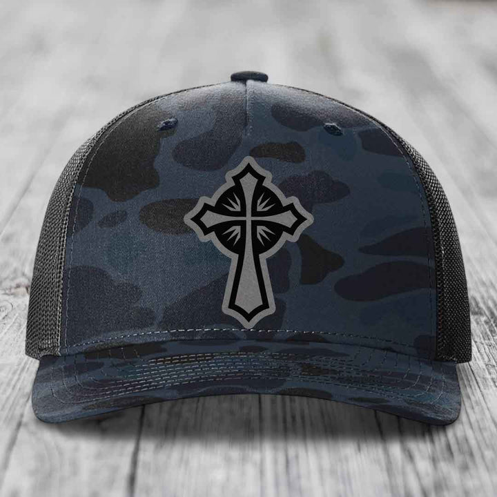 Camouflage trucker hat with a grey and black cross patch on the front.
