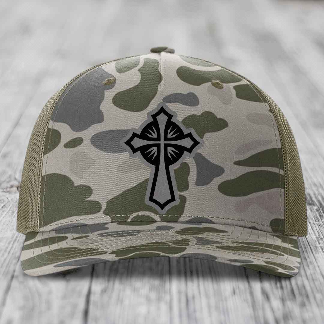Camouflage trucker hat with black cross patch on front, olive green mesh back.