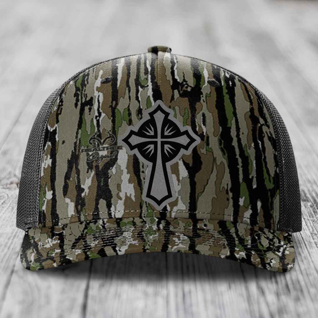 Camouflage trucker hat with black and grey cross patch on front.