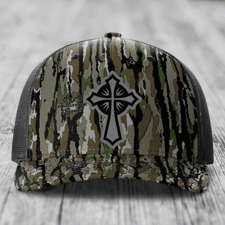 Camouflage trucker hat with black and grey cross patch on front.