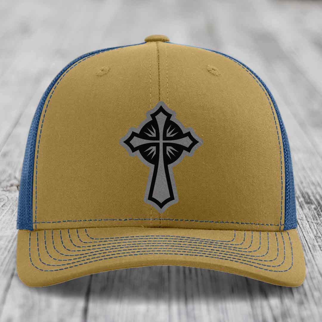 Tan and blue trucker hat with a black and grey cross patch on the front.