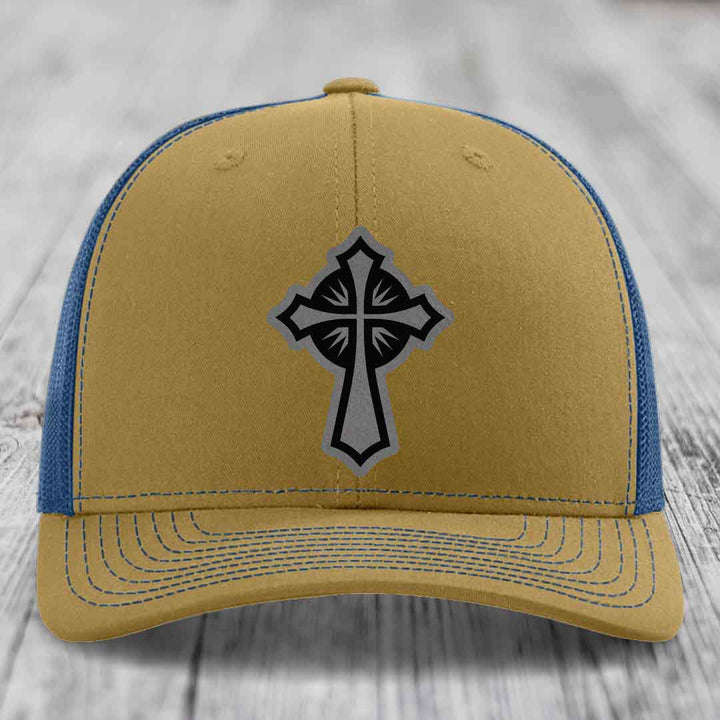 Tan and blue trucker hat with a black and grey cross patch on the front.