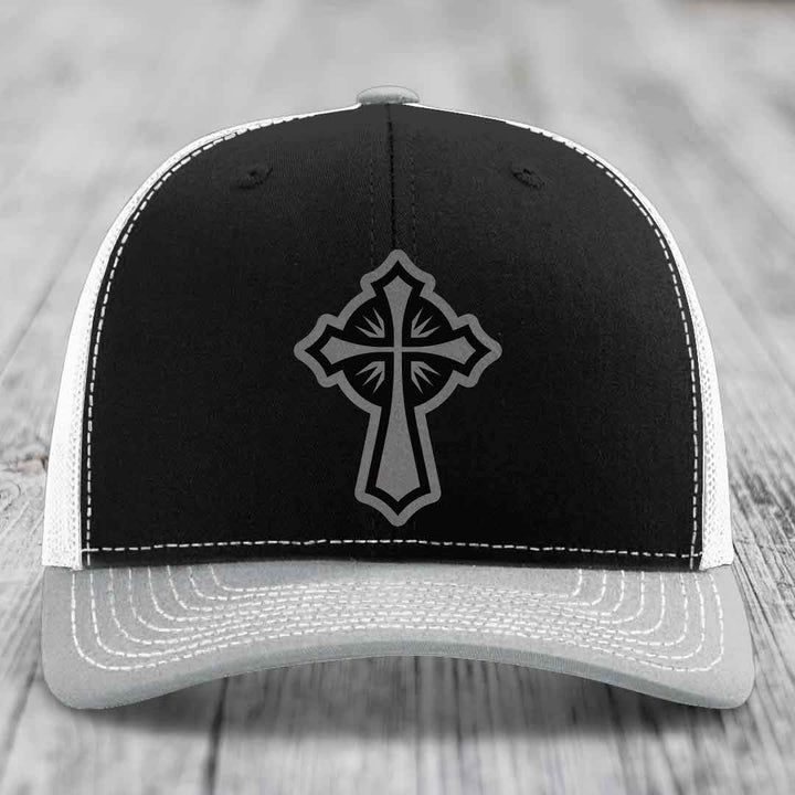 Black trucker hat with grey cross patch and white stitching on front panel.