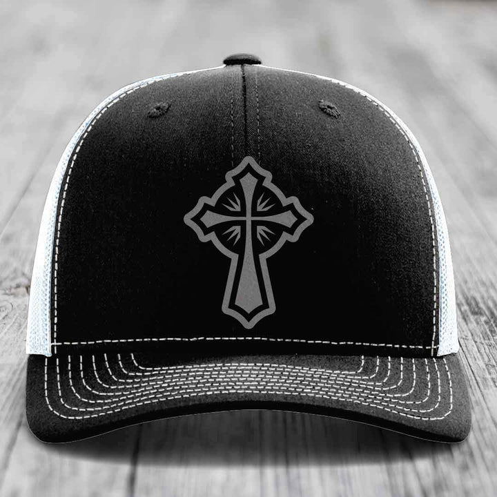 Black trucker hat with grey cross patch and white stitching on front panel.