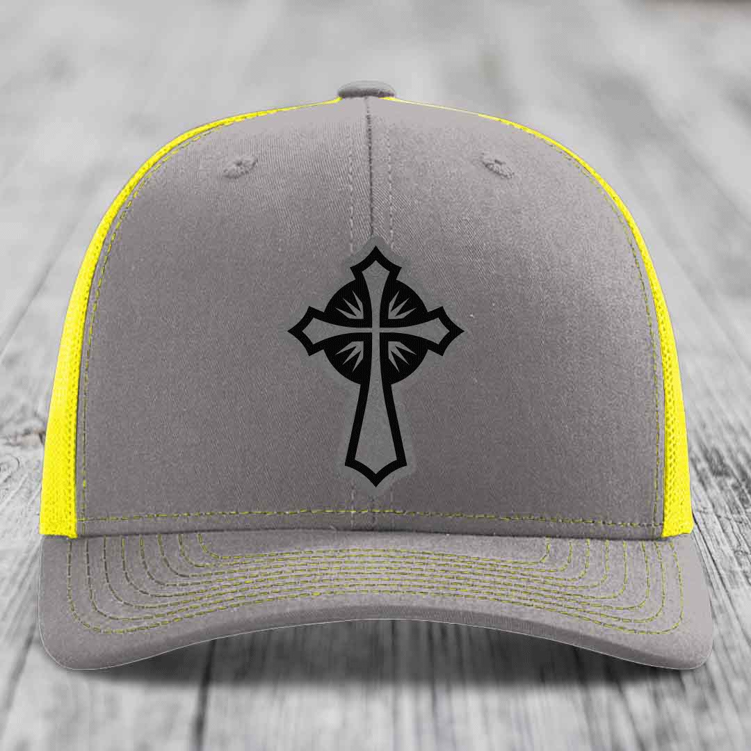 Grey trucker hat with black cross patch and yellow mesh sides and stitching.