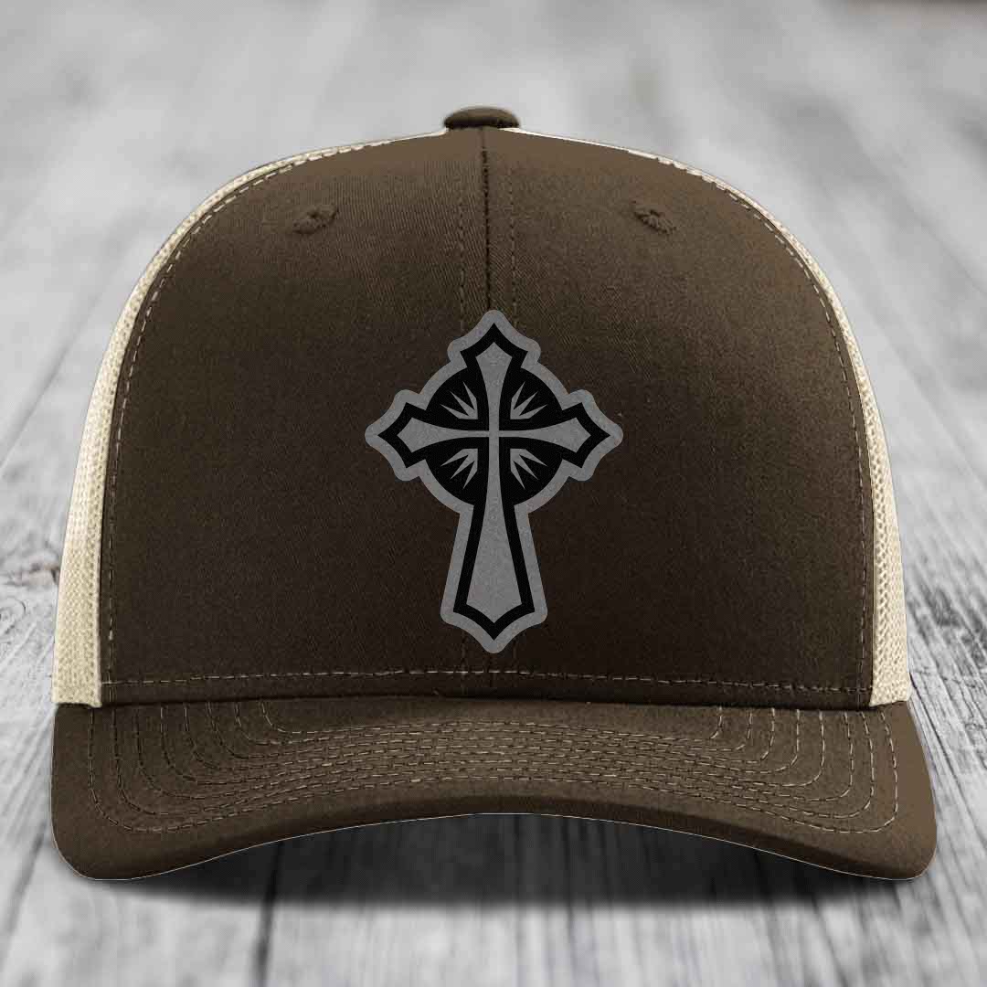 Brown trucker hat with black and grey cross patch on front, cream mesh sides.