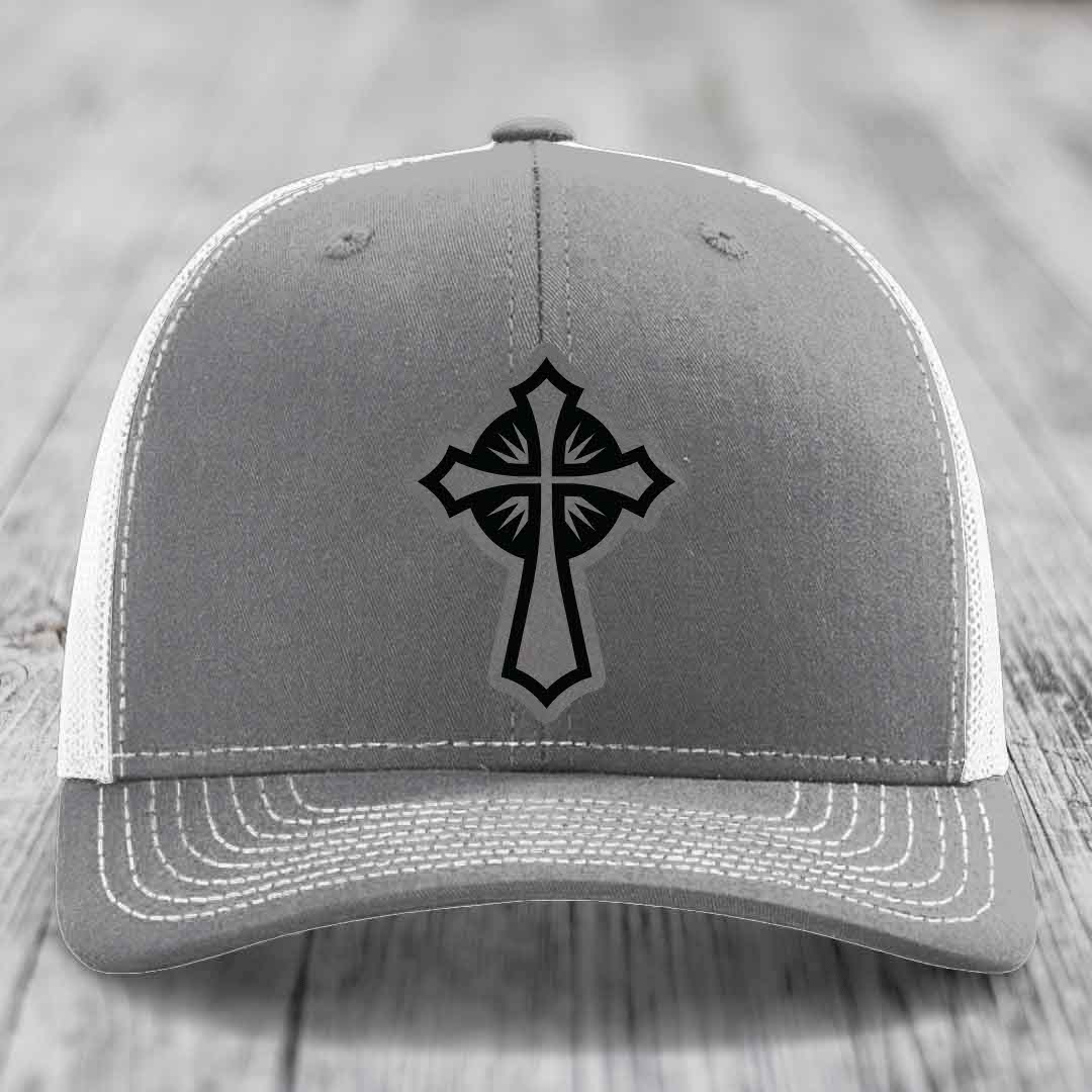 Grey trucker hat with black cross patch on front, white mesh back and white stitching.