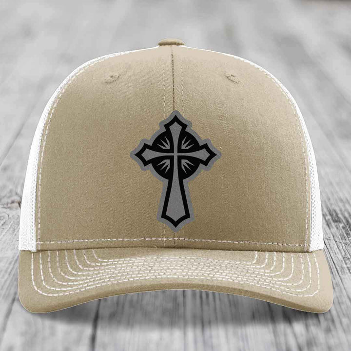 Tan trucker hat with black and grey cross patch on front, white mesh back and stitching.