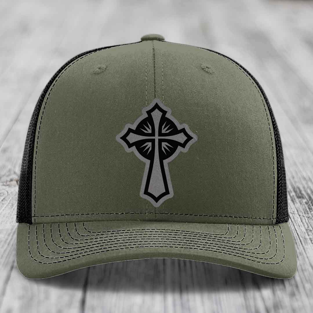 Olive green trucker hat with black cross patch on front, black mesh back.