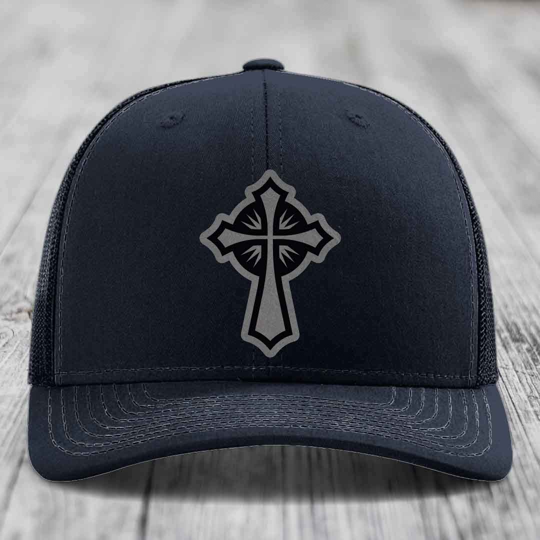 Black trucker hat with grey and black cross patch on front, light stitching, wood background.