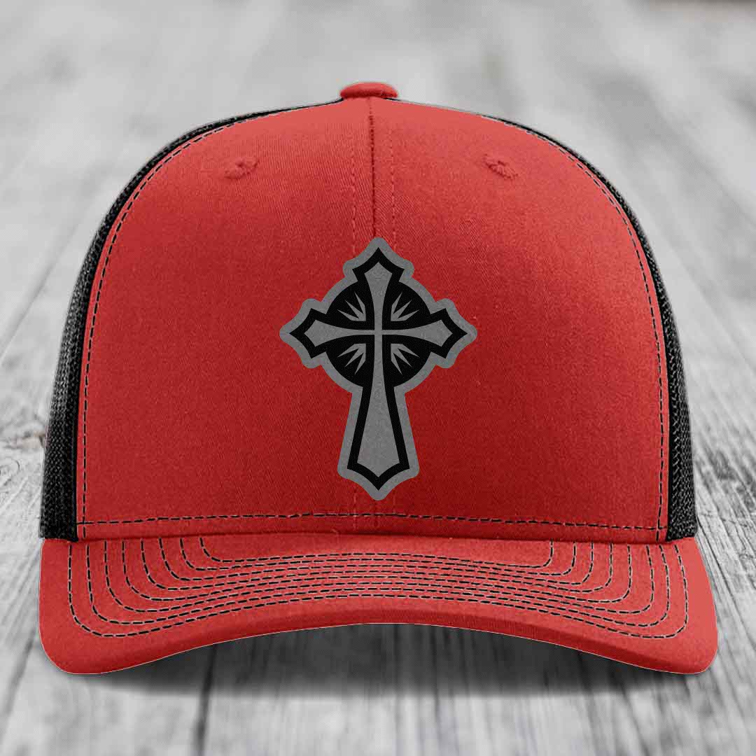 Red trucker hat with black and grey cross patch on front, black mesh back.