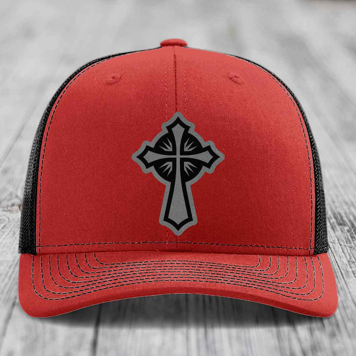 Red trucker hat with black and grey cross patch on front, black mesh back.