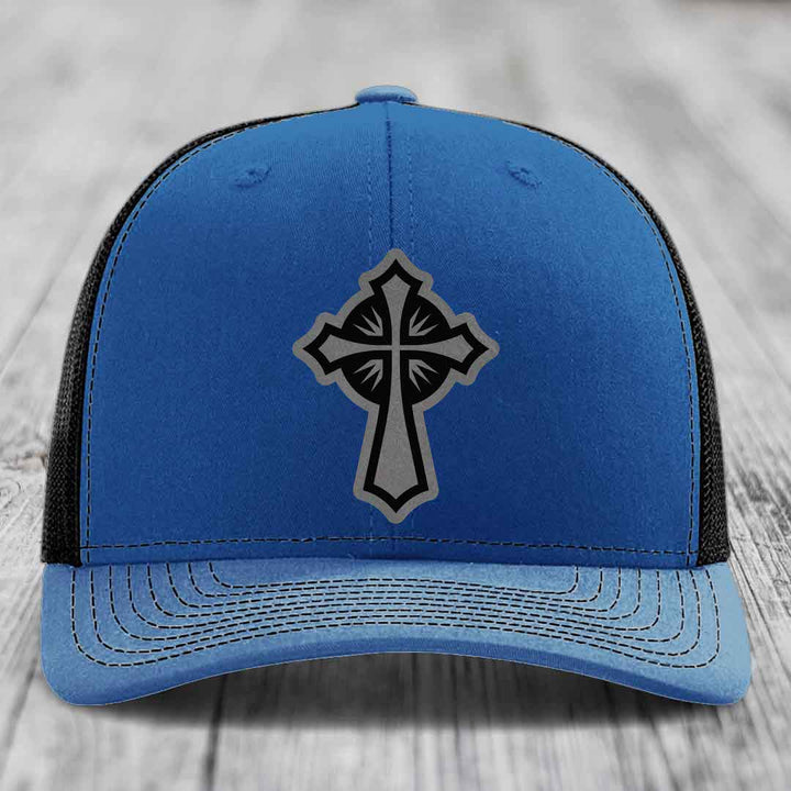 Blue trucker hat with black and grey cross patch on front, black mesh back.