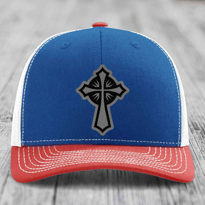 Blue and red trucker hat with a grey and black cross patch on the front.