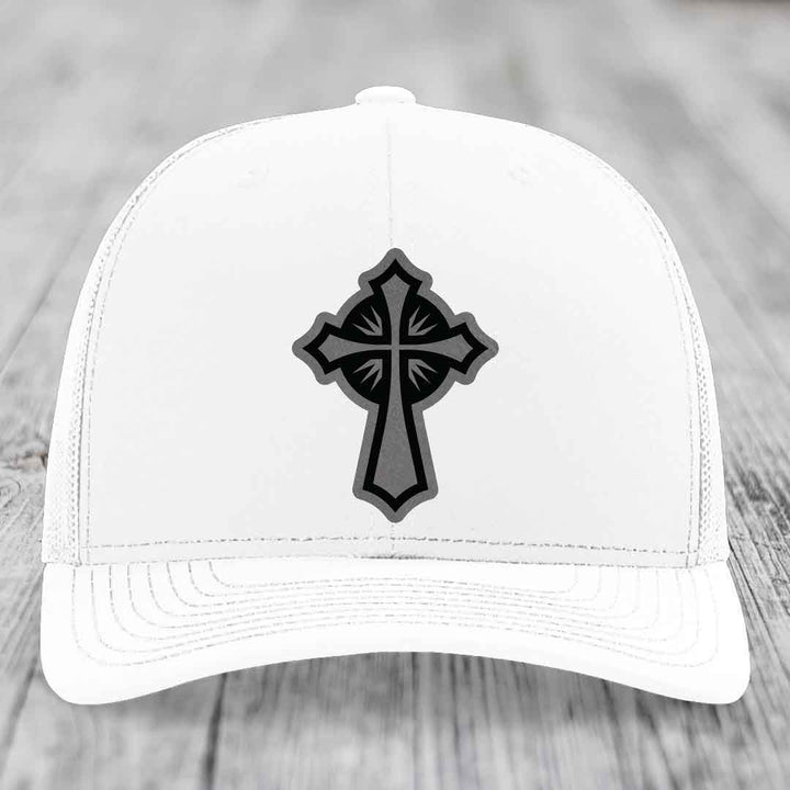 White trucker hat with black and grey cross leather patch on front.