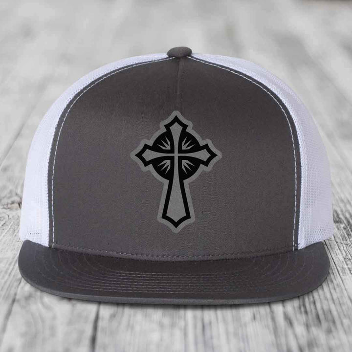 Grey and white trucker hat with black cross patch on front.