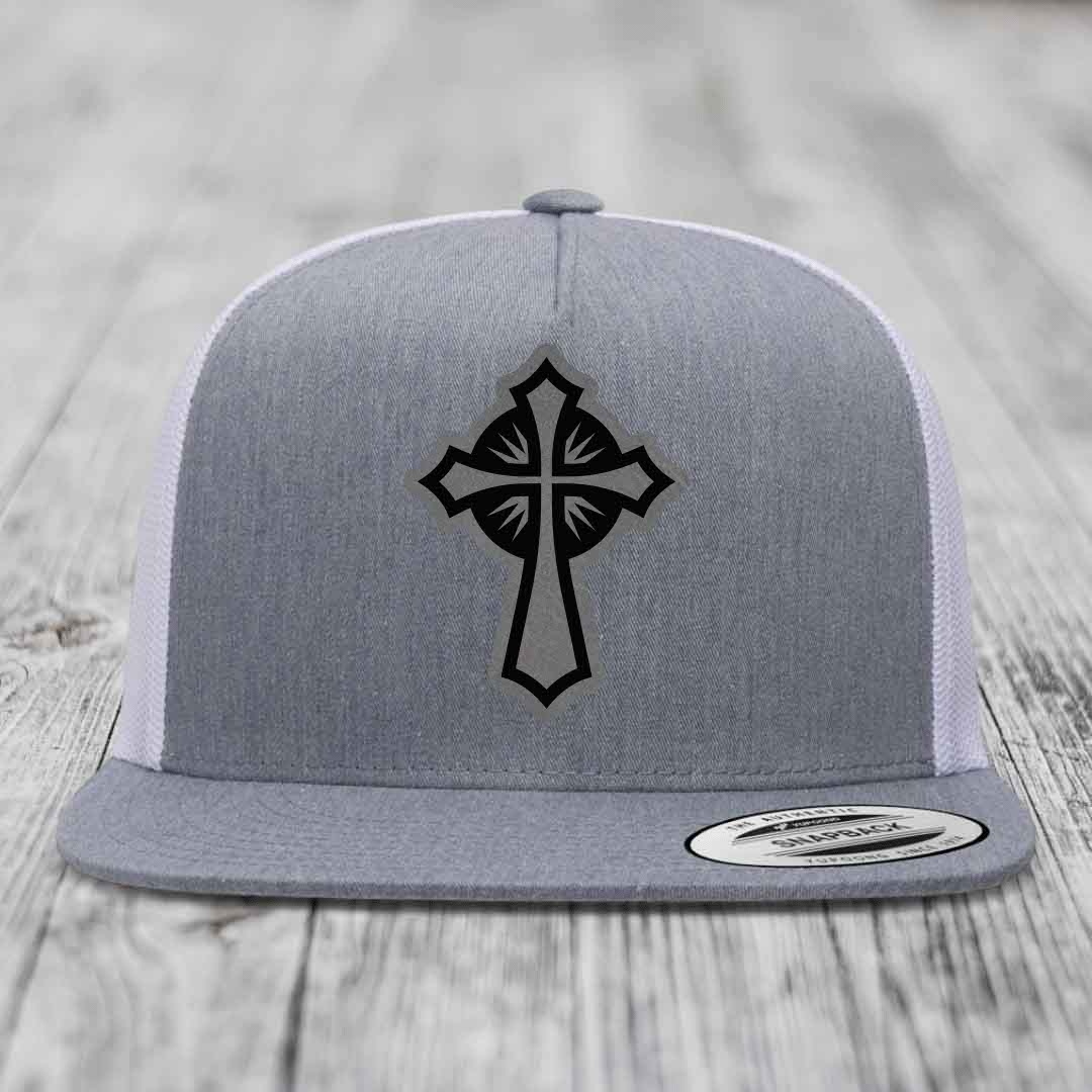 Grey trucker hat with black cross patch on front, white mesh back, flat brim.