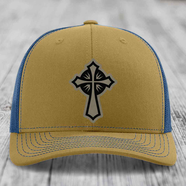 Tan and blue trucker hat with a black cross patch on the front.