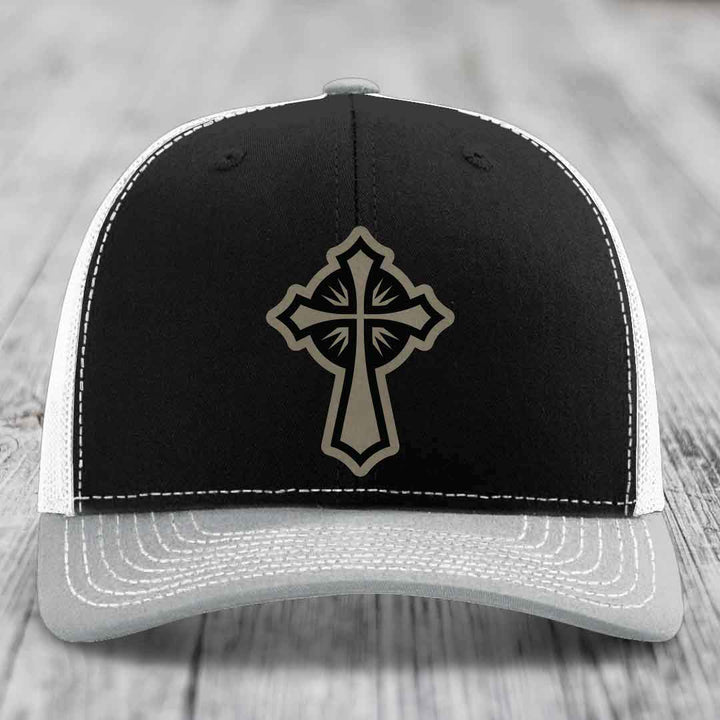 Black trucker hat with grey cross patch and white stitching on front panel.