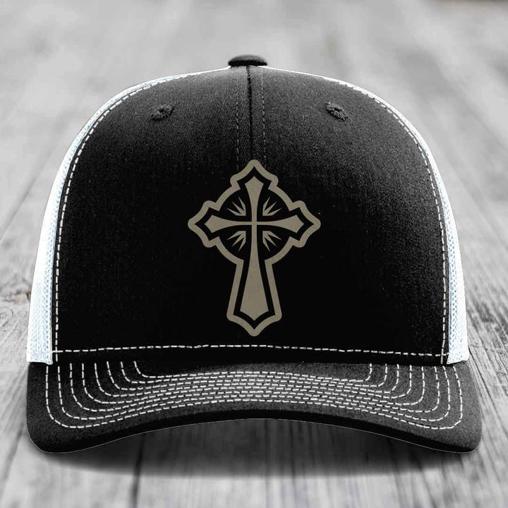 Black trucker hat with grey cross patch and white stitching on front panel.