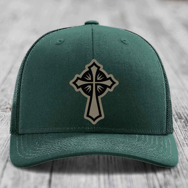 Dark green trucker hat with a cross patch on front, featuring black and beige design.