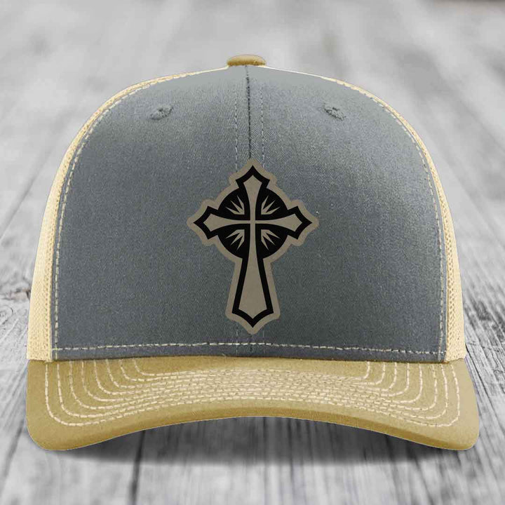 Grey and beige trucker hat with black cross leather patch on front.