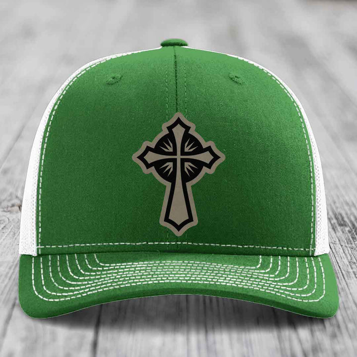 Green trucker hat with black and tan cross patch on front, white mesh back and white stitching.