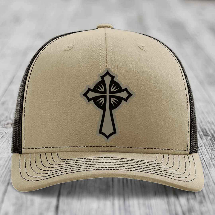 Beige trucker hat with black cross patch on front, black mesh back and stitched brim.