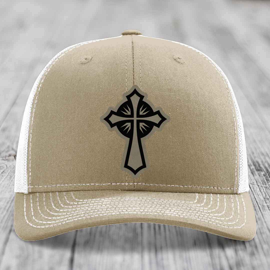 Tan trucker hat with black cross patch on front, white mesh back and white stitching.