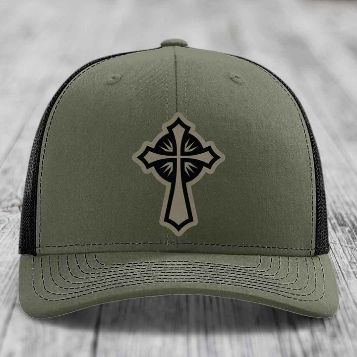 Olive green trucker hat with black cross patch on front, black mesh back.