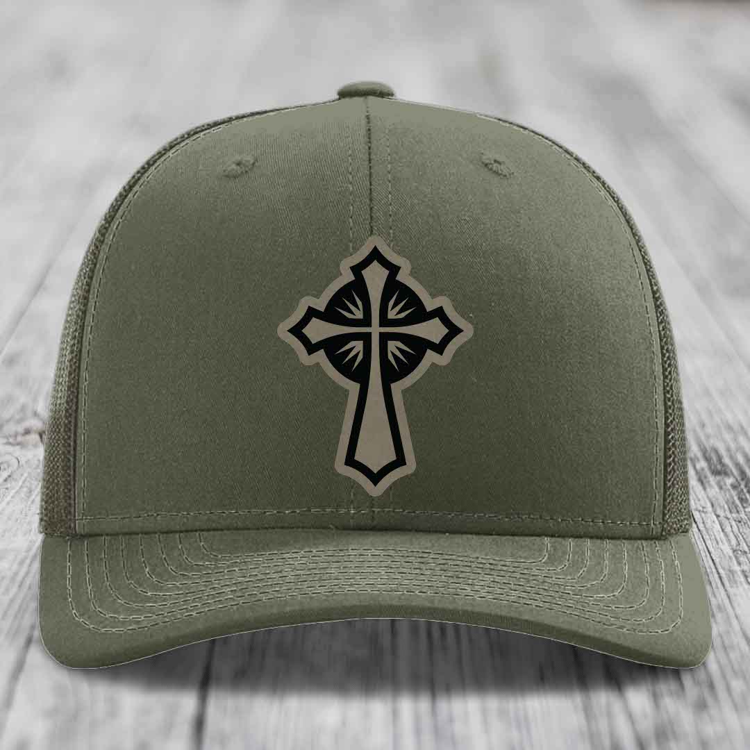 Olive green trucker hat with black and beige cross patch on front.