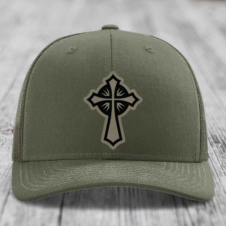 Olive green trucker hat with black and beige cross patch on front.