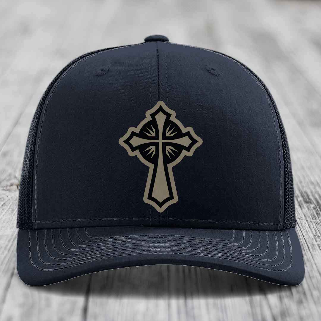 Black trucker hat with a beige cross patch on the front, placed on a wooden surface.