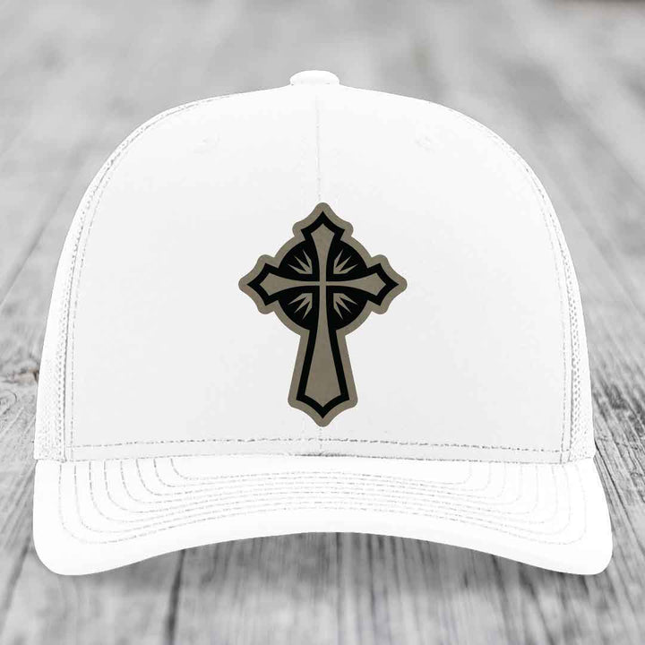White trucker hat with a black and grey cross leather patch on the front.