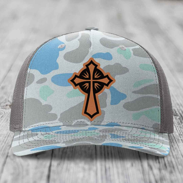 Camouflage trucker hat with brown cross leather patch on front.