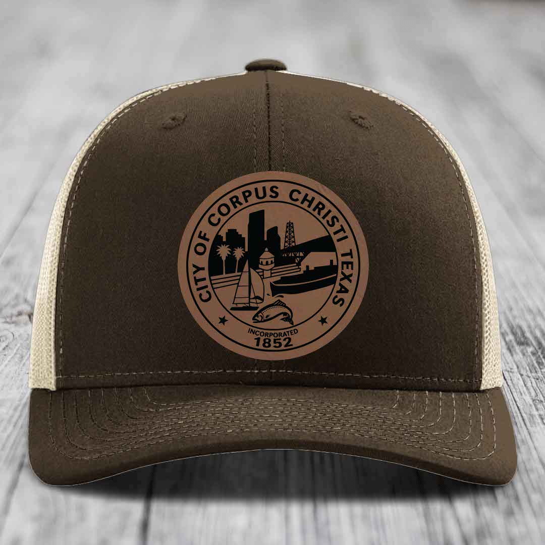 Brown trucker hat with beige mesh back and a circular leather patch featuring the City of Corpus Christi, Texas seal.