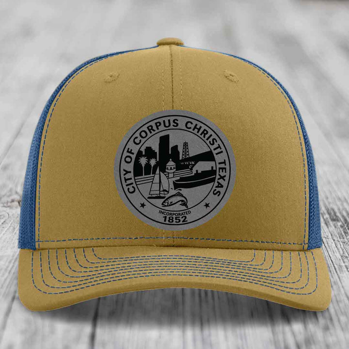 Tan trucker hat with blue mesh back and gray circular Corpus Christi Texas seal patch.
