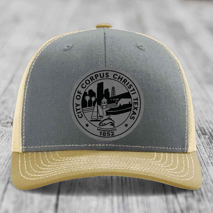 Grey and beige trucker hat with Corpus Christi Texas seal patch on front.