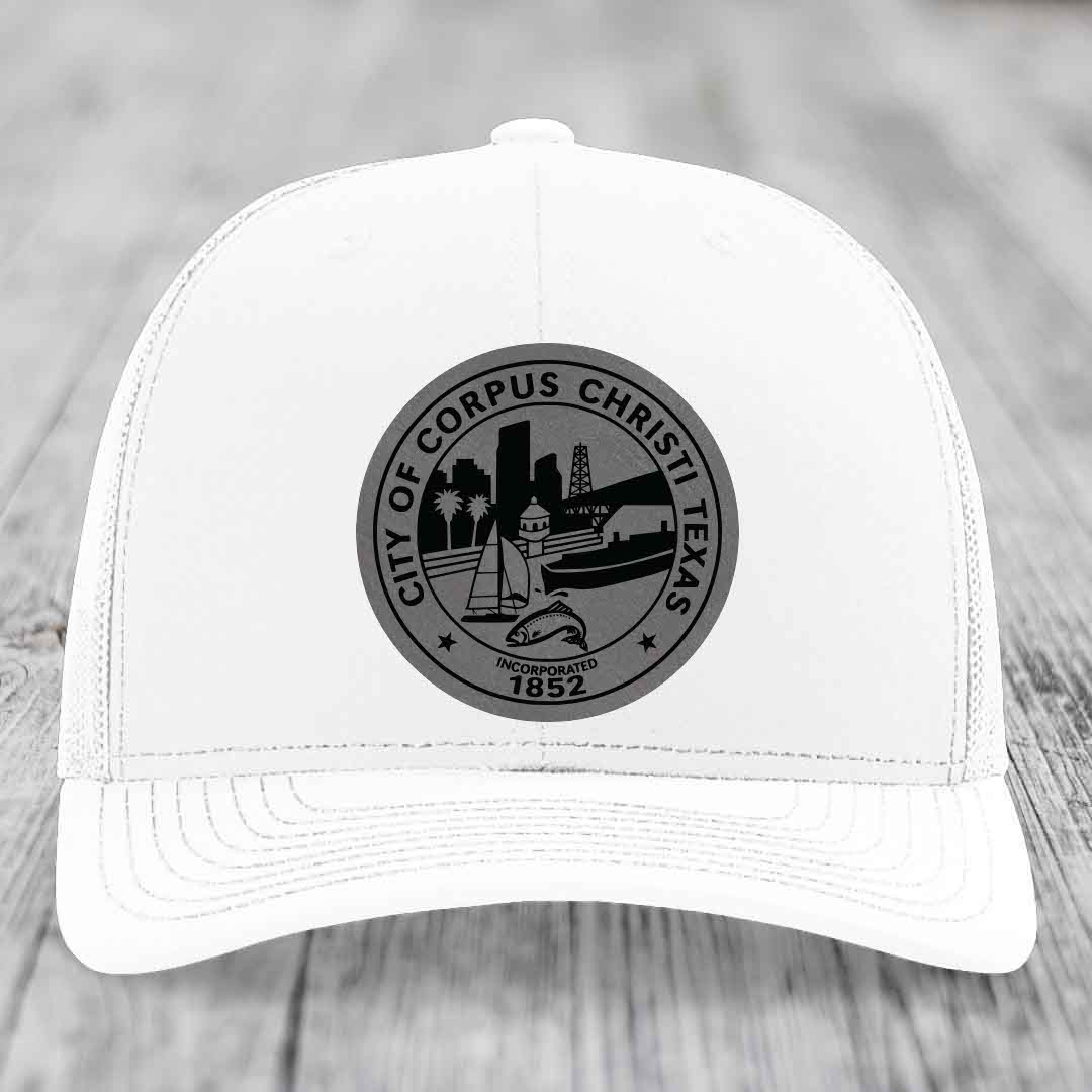White trucker hat with grey Corpus Christi Texas city seal patch on front.