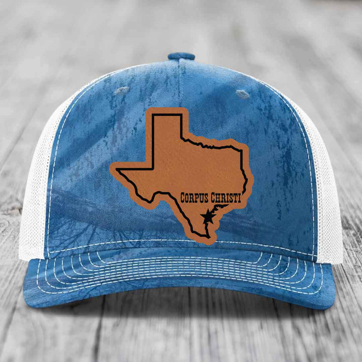 Camouflage trucker hat with brown leather patch shaped like Texas, labeled &