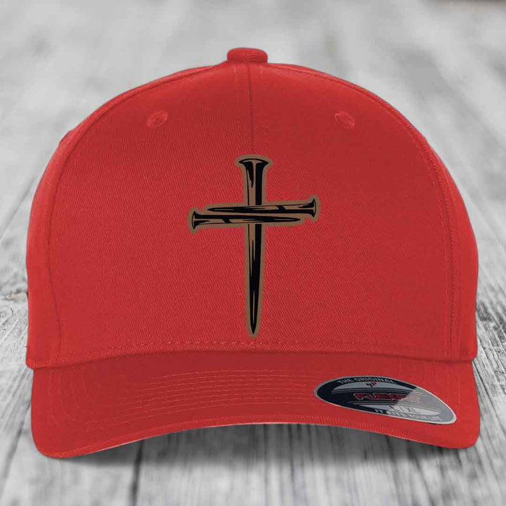 Black baseball cap with a cross made of nails patch on front, displayed on wooden surface.