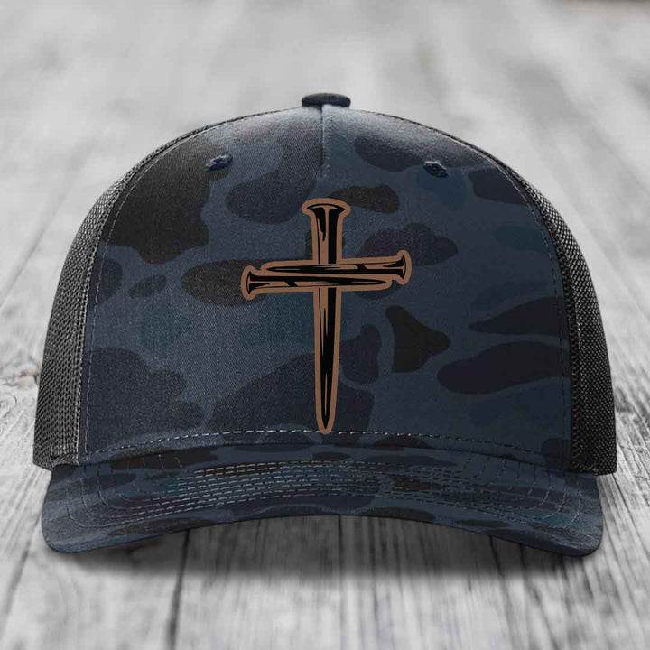 Camouflage trucker hat with a cross made of nails patch on front.