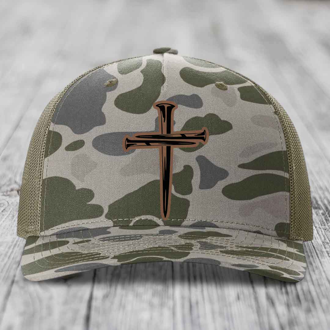 Camouflage trucker hat with a cross of nails leather patch on front.
