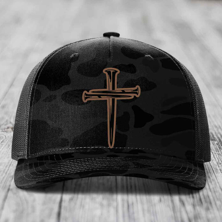 Camouflage trucker hat with a cross made of nails patch on front.