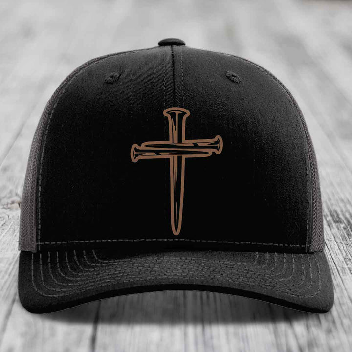 Black trucker hat with brown cross of nails patch and white stitching on front panel.