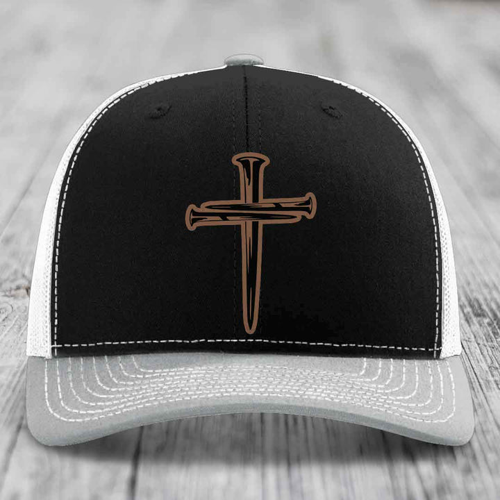 Brown trucker hat with cross of nails patch and white stitching on front panel.