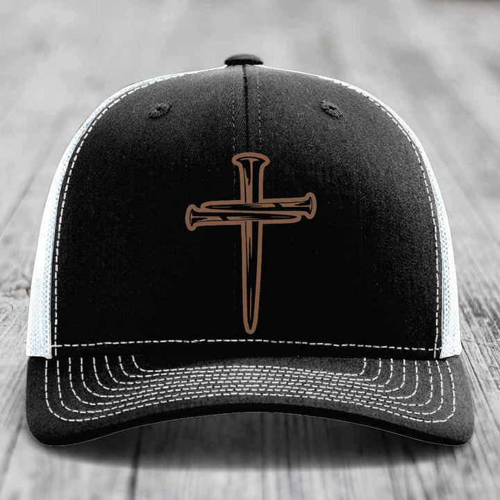 Black trucker hat with brown cross of nails patch on front, white mesh back and gray brim.