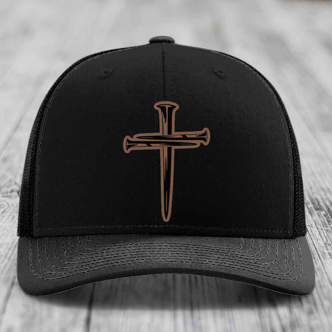 Tan baseball cap with blue mesh back and black cross made of nails patch on front.